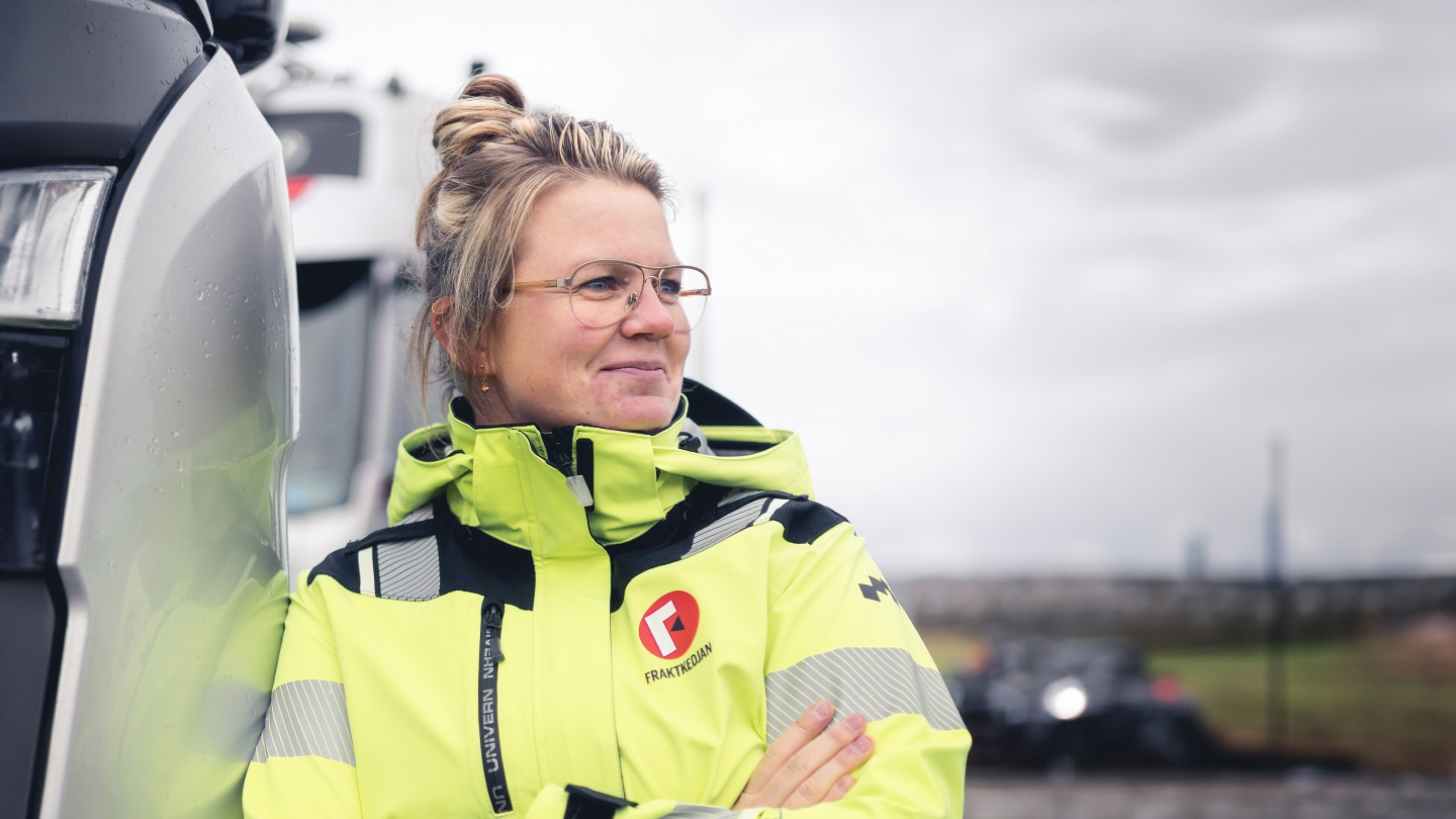 Annika Persson, avslappnat lutad mot förarhytten på en lastbil.